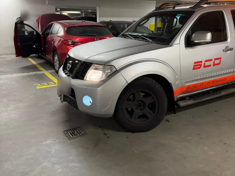 Pick-up BCD dans un parking souterrain à Bruxelles, à côté d'une voiture en panne capot ouvert